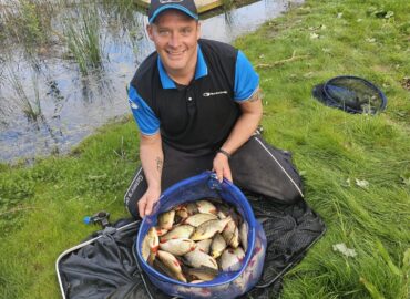 Man holding a net filled with freshly caught fish by a lake, showcasing the free fishing opportunity available at Woodland Lakes Holiday Lodges.