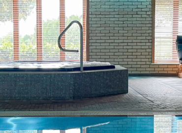 Indoor health spa featuring a relaxing hot tub with a handrail, surrounded by large windows overlooking greenery, enhancing the luxurious atmosphere for guests at Woodland Lakes Holiday Lodges.