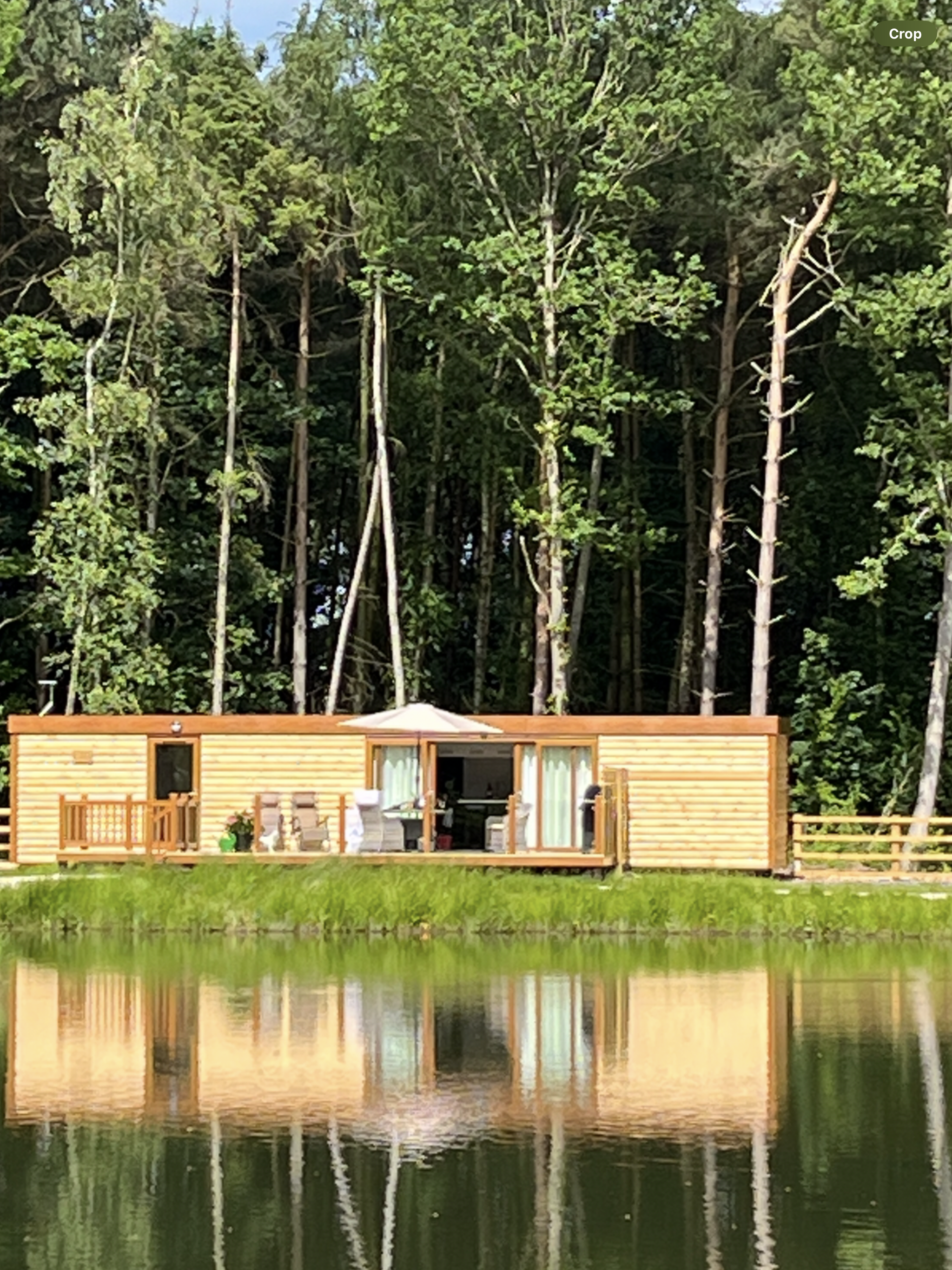 Dog-friendly lodge overlooking a serene lake, surrounded by lush trees, featuring outdoor decking and spa amenities, ideal for couples seeking relaxation at Woodland Lakes in Yorkshire.