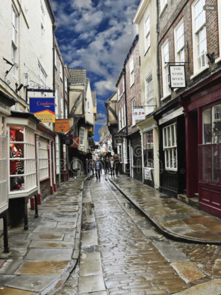 Historic cobbled street in York, lined with charming shops and cafes, under a dramatic cloudy sky, showcasing the city's rich heritage and inviting atmosphere for visitors exploring local culture.
