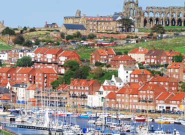 Coastal view of Whitby featuring colourful houses, a marina with moored boats, and the historic Whitby Abbey in the background, highlighting the charm of Yorkshire's seaside attractions.