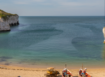 Coastal view featuring fishing boats on sandy beach, cliffs in background, and clear blue water, ideal for romantic getaways near York.