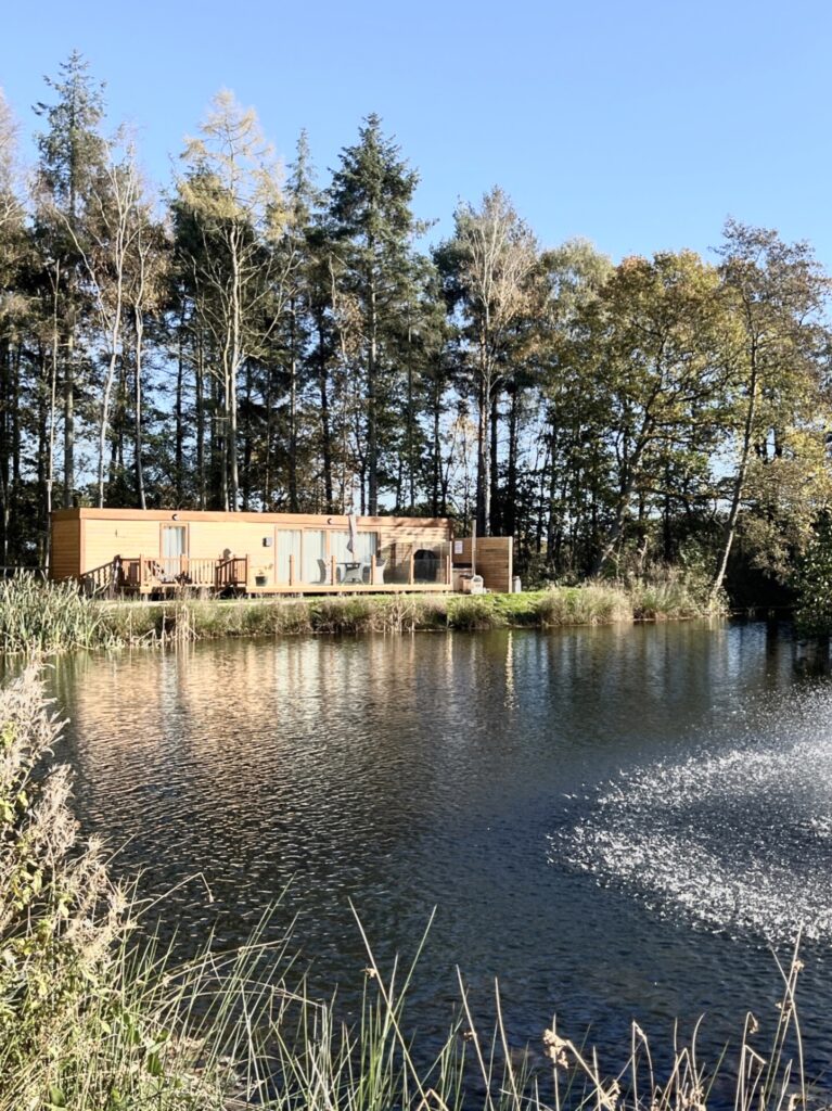 Lodge with hot tub by tranquil fishing lake surrounded by trees at Woodland Lakes Holiday Lodges in Yorkshire.