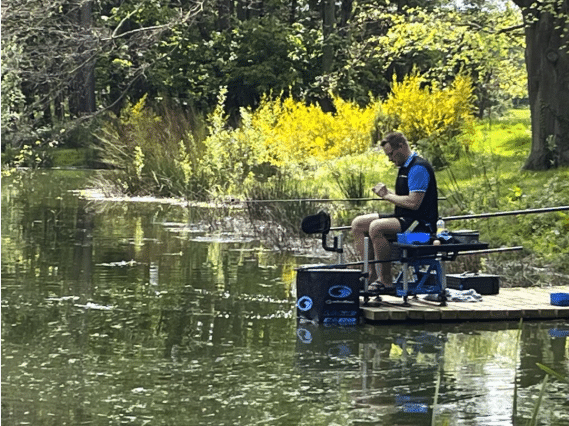 Person fishing from a platform by a tranquil lake surrounded by lush greenery, ideal for a peaceful getaway at Woodland Lakes Holiday Lodges in Yorkshire.