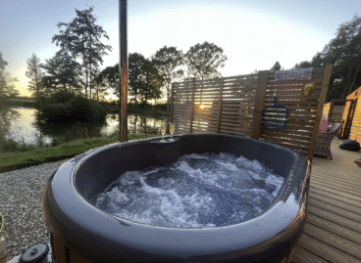 Hot tub with bubbling water on a wooden deck overlooking a tranquil lakeside view, surrounded by trees at sunset, ideal for a relaxing dog-friendly holiday near York.