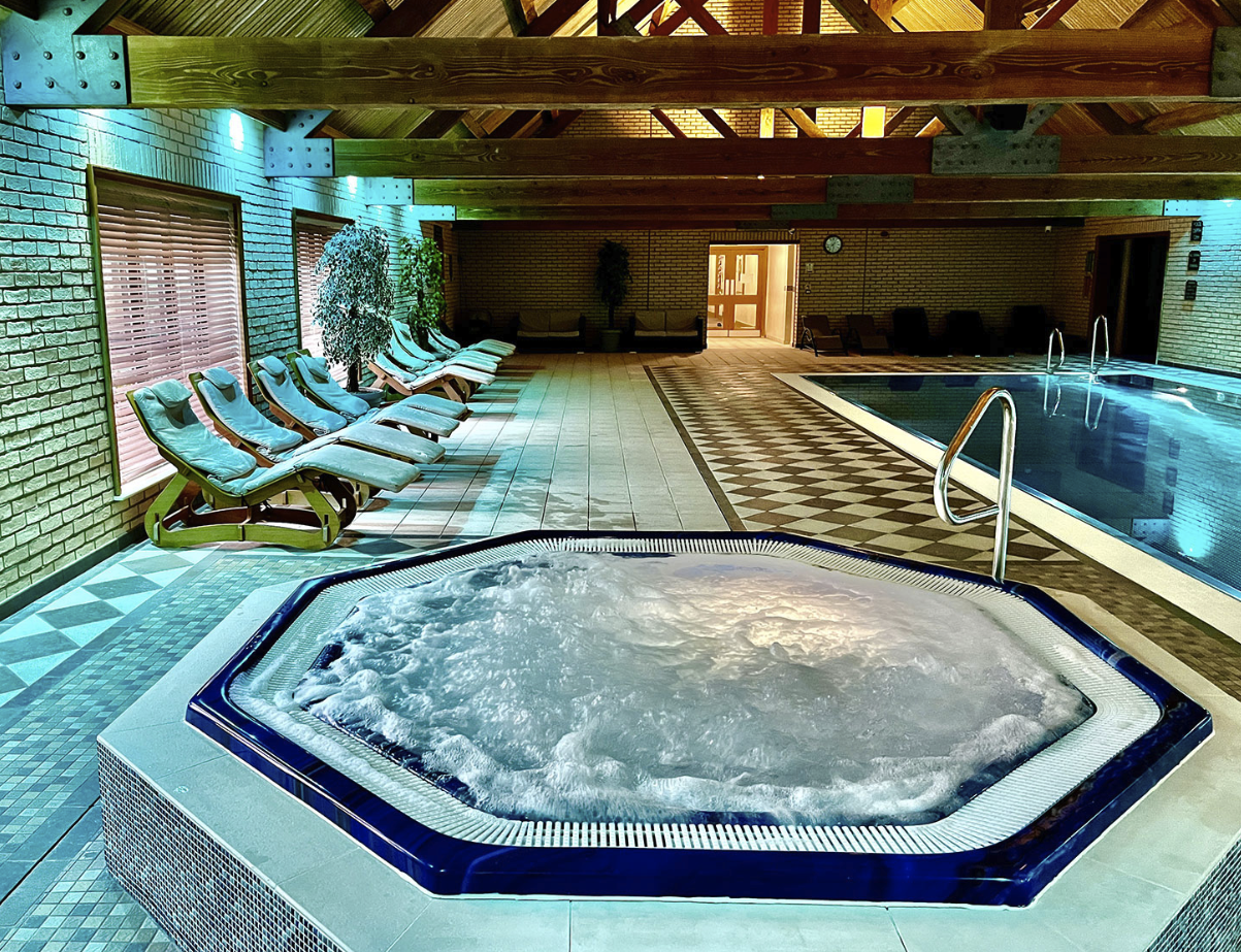 Indoor hot tub with bubbling water, surrounded by lounge chairs and a swimming pool, in a luxurious spa setting at Woodland Lakes Holiday Lodges near York.
