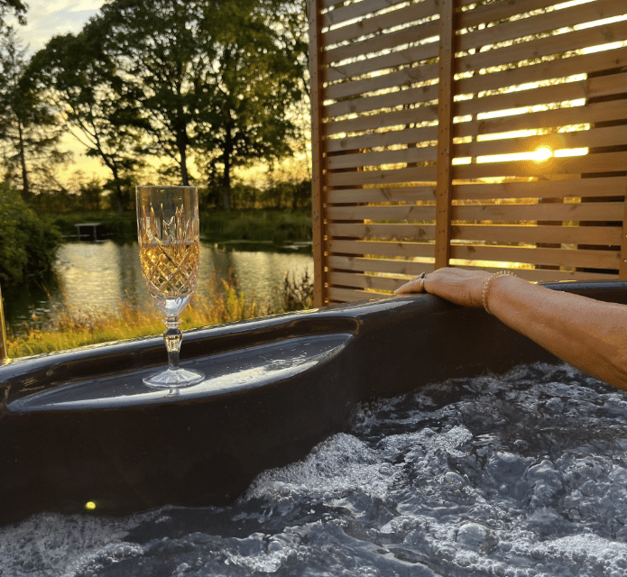 Luxury hot tub lodge with a glass of champagne, surrounded by serene woodland and a sunset view, emphasizing relaxation and wellness in Yorkshire.