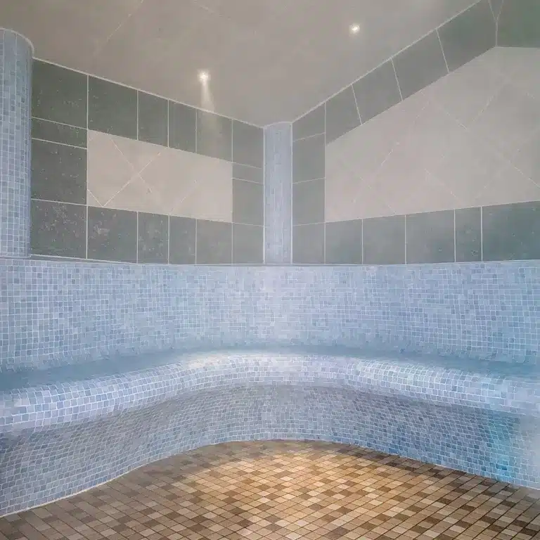 Steam room with tiled benches and mosaic flooring, part of the spa facilities at Woodland Lakes, promoting relaxation and wellness for guests.